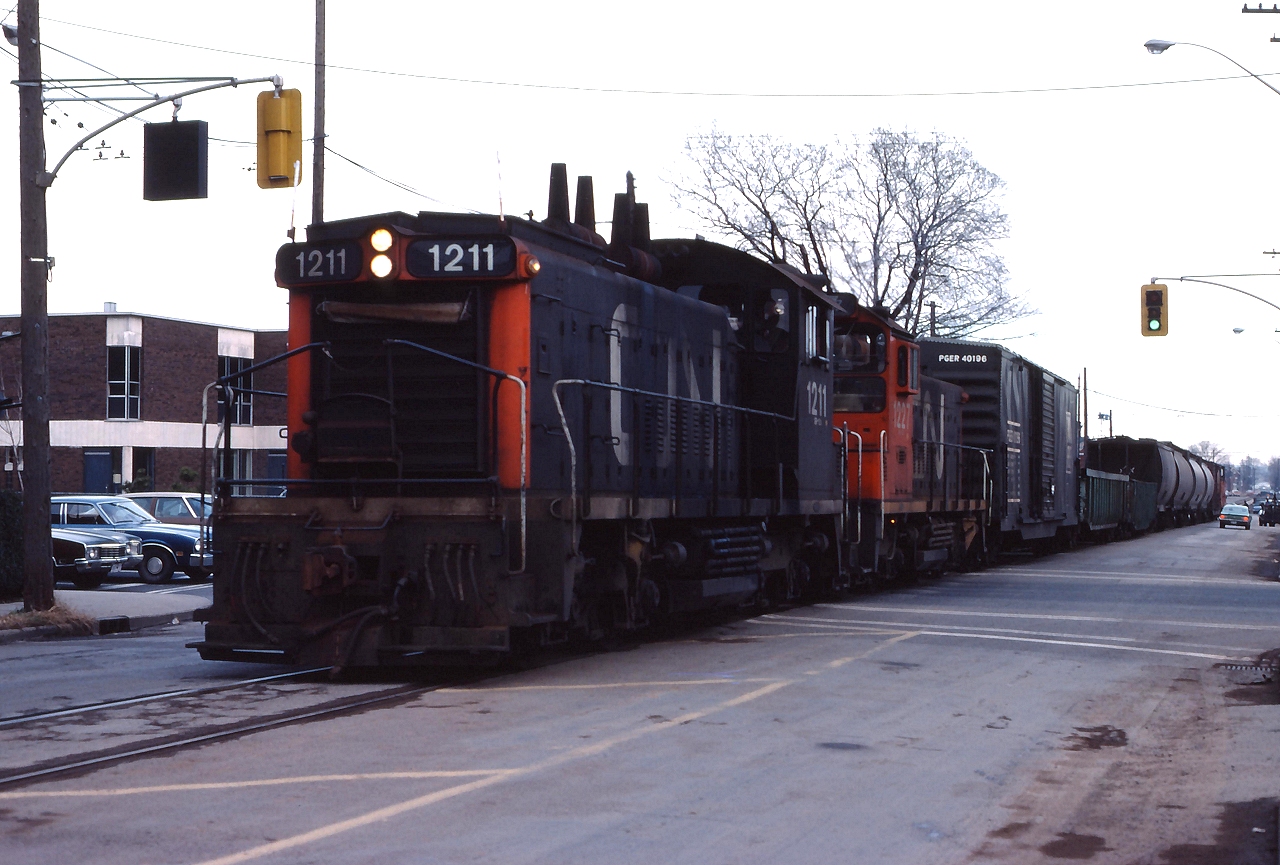 CN 1211 and CN 1227 take train 535 down Ferguson Avenue in Hamilton on a dreary December day in 1975