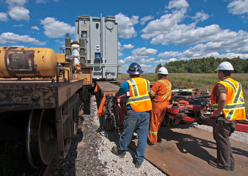 After being called for as a conductor on a  L351 this morning out of MacMillian Yard, I decided sure, why not, I'll being the camera with me. Turns out we had to take a D1R transformer 42 miles where it was to be off loaded onto truck then taken the rest of the way to the hydro substation just down the road off of Tremaine Rd in Oakville. Here crews from Don Anderson are using hydraulic jacks (not seen) to push the transformer from flat car to flat bed as workmen watch on.