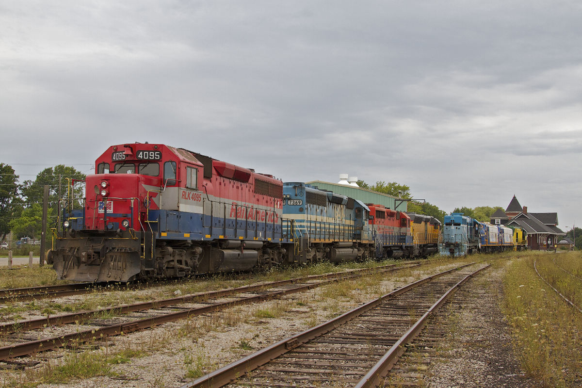 A bright line of locomotives rest in GEXR's Goderich yard on a gloomy August day, while the old station is seen in the background.