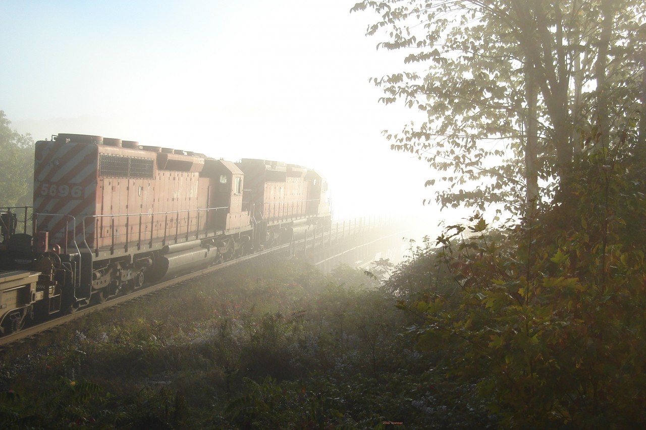 A sunny, bright September 21, 2006 early morning and a dense fog/mist rises from Mud Lake.  CP #152 with 5949 & 5696 heads into the abyss onto Mud Lake Trestle , mp 27.4 of the Belleville Sub