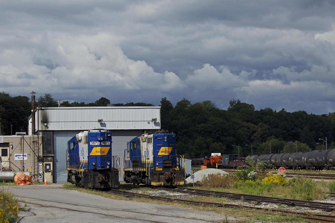 Under threatening skies, RLK 3873 and another geep sit quietly outside the Stuart Street engine shops. A Schnabel car belonging to Hydro One can be seen in the background with a string of cars.