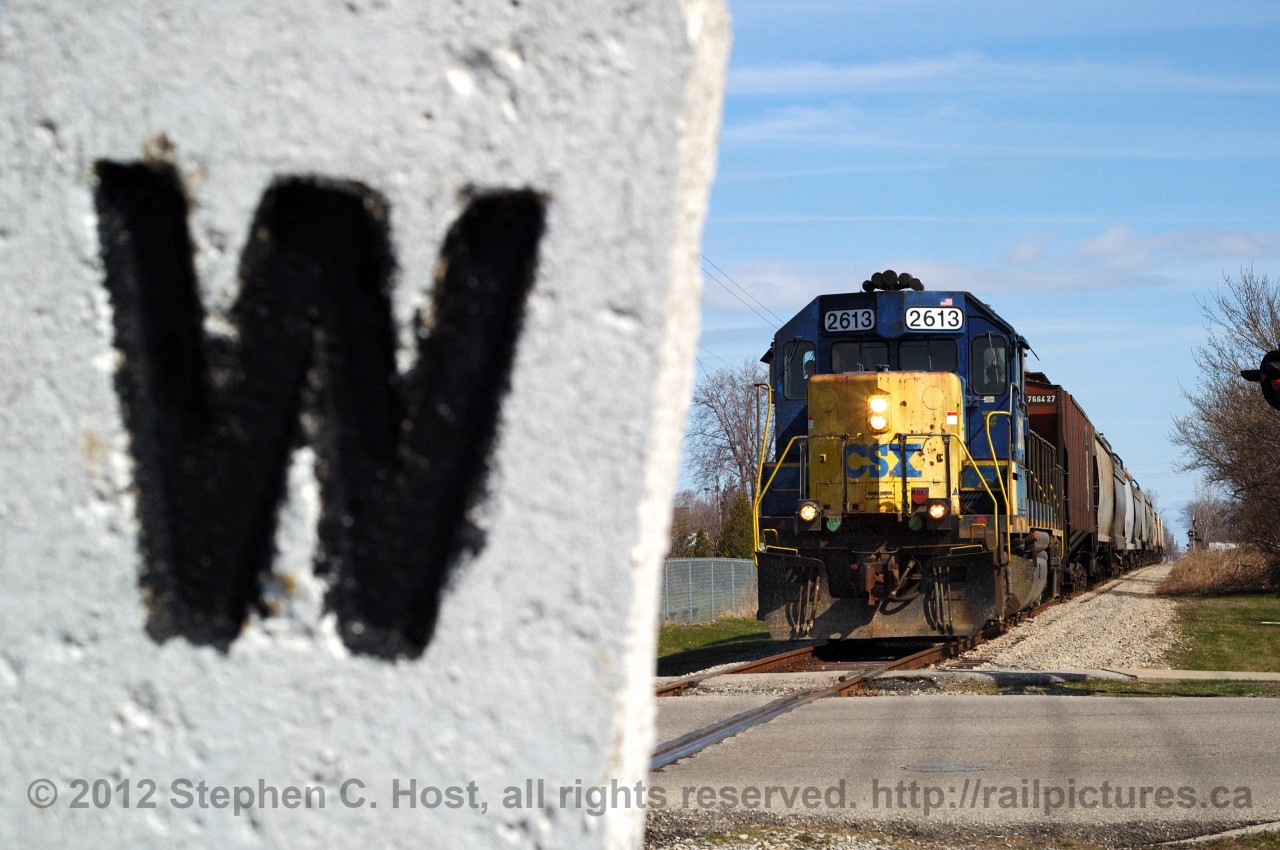 CSX D924 is seen heading south on the Sarnia sub with grain cars for Tupperville and Wallaceburg. Framed in the photo is a concrete whistle post, which may date to the predecessors of this railway (Erie & Huron, Lake Erie & Detroit River Railway, or Pere Marquette).  Despite the railway being in the transfer/discontinuance process since 2006, this local still runs twice per week and run as far as Dresden, Ontario.