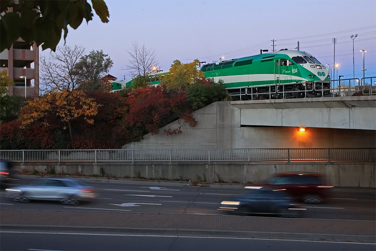 In the pale pre-dawn light a GO train waits for departure on Track 4 at Oakville Station as traffic on Trafalgar Road whizzes by below.