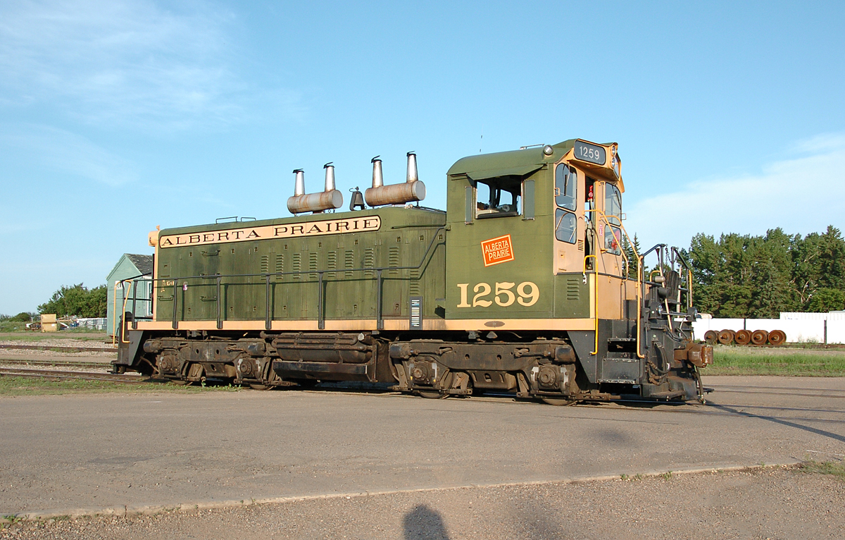 APXX 1259, an ex-CN GMD SW1200RS backs across the "yard" crossing in Stettler to couple with its train and pull it across the crossing.