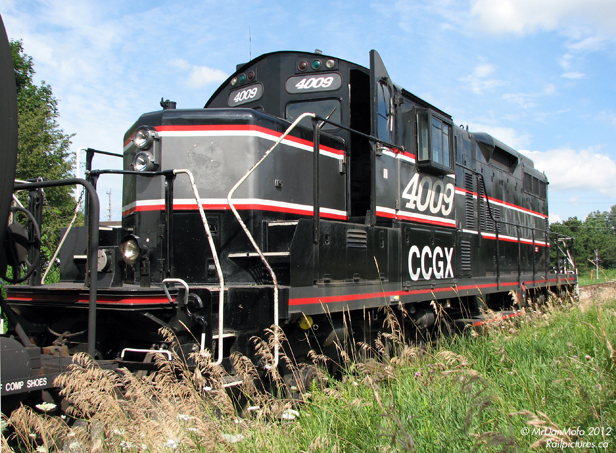 New delivery. Just arrived off CP this past week, the Orangeville-Brampton Railway's new locomotive sits on the weedy interchange track in Streetsville awaiting the biweekly local to arrive and pick her up for the trip back to Orangeville. CCGX 4009 originally started off as a plain-jane CN GP9 built by GMD London. After she was rebuilt as 4127 in the 80's, she continued in service until retired and sold to Canadian Railserve. Cando Contracting eventually picked her up for their Athabasca Northern Railway operations (if one looks closely, they can see the former ANY logos with the wolf on the nose). When CN took ANY over, 4009 was reassigned the OBRY to replace their aging non-rebuilt ex-QNSL GP9, which, as this photo was taken, was on its way south to meet 4009 for the first time.