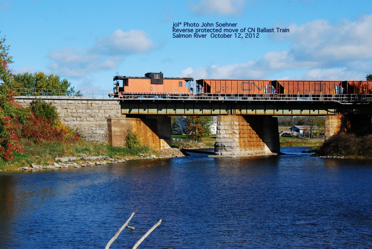 A CN Ballast Train in a reverse move backs along the Third Rail dropping ballast at various sites.  A CN worker on the caboose in radio contact with the engineer calls out instructions to the front end as the train approaches Milltown Road crossing.