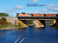 A CN Ballast Train in a reverse move backs along the Third Rail dropping ballast at various sites.  A CN worker on the caboose in radio contact with the engineer calls out instructions to the front end as the train approaches Milltown Road crossing.  