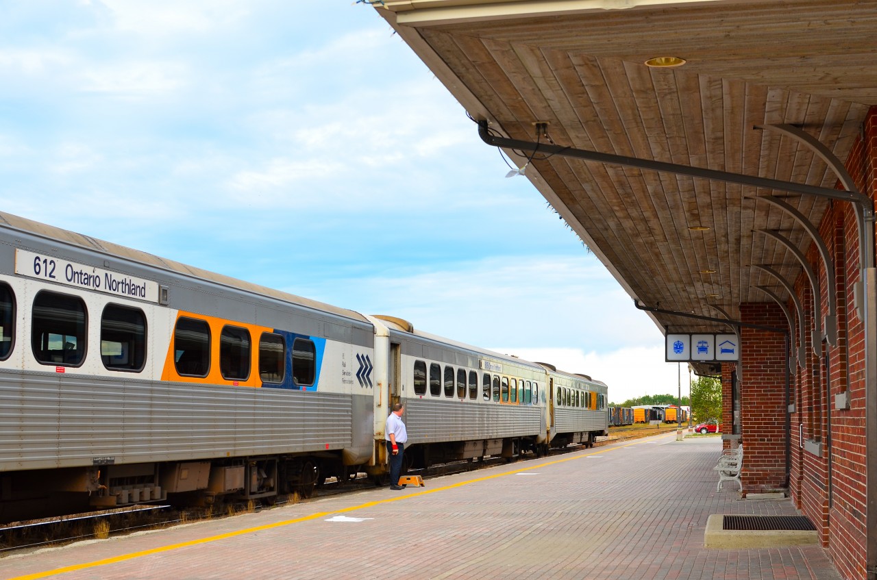 The southbound Northlander (Train 698) at Cochrane, nine minutes before departure. Most passengers are already on board the two coaches. The diner (last car) will open soon after departure. The sign above the station entrance has symbols for three services available but omits the restaurant. The icon for passenger service remains the now rare “A” unit. The freight shed is visible in the distance.