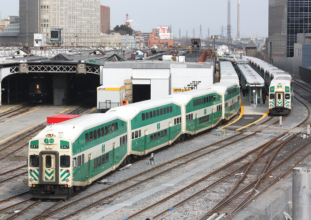 GO cab car 247 leads Barrie-bound train 801 out of the south end of Toronto's Union Station. To the right, 233 is waiting to depart with a Milton-line train on platform 27. Tracks 11 & 12 of the train shed are undergoing renovations as part of GO Transit's station modernization program. In the distance on the right, Scott St. interlocking tower can also be seen, along with the smokestacks of power generation plants off in the Portlands.