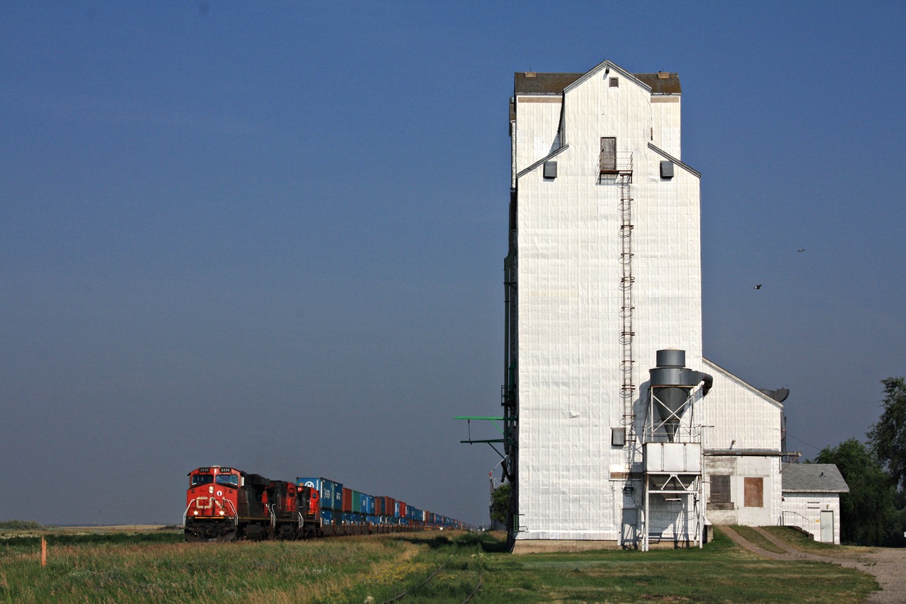 CN eastbound intermodal with three GE's roars by Rivers Manitoba's elevator.