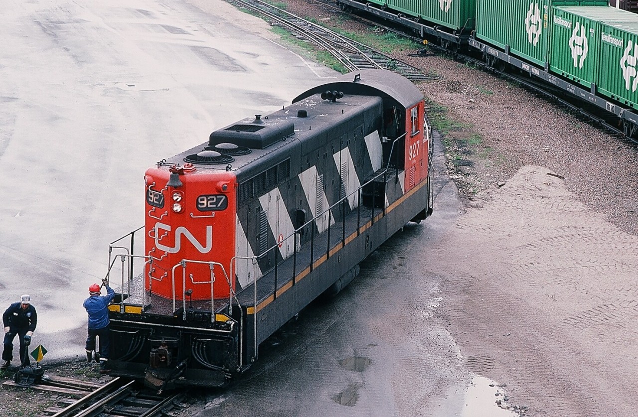 A special place – The Rock. August 2, 1982. Port-aux-Basques, Newfoundland. Need road freight power?  Require passenger train power?  Road Switcher work to do?  Have a need for yard power?  One unit type will do it: GMD's NF series. 1200 HP. Six traction motors. Short wheelbase. Oh, minor detail: track gauge is 42 inches. Terra Transport #927, in CN zebra stripes, is on yard duty today.  What's interesting: One of fourty seven ubiquitous GMD NF210 (& 110) locomotives built by GMD 1952 through 1960 for the CN Newfoundland narrow gauge railway.  Today 927 is now Nigeria 1161.  Note the dual gauge trackage. Terra Transport was ahead of its time, most LCL (less than carload) freight was containerized.  Some history: In 1979, all of CN's freight railway operations on Newfoundland, along with the CN Roadcruiser Bus service and CN's trucking operation, were placed into a new division named Terra Transport. On June 20, 1988, it was officially announced that the railway would cease operations as of September 1, 1988. Some freight trains still ran until late September, with the last scheduled run on September 29, 1988. The last scheduled passenger train ran on September 30, 1988, from Bishops Falls to Corner Brook. Some salvage trains were still operating in the summer of 1990.  Kodachrome by S.Danko.