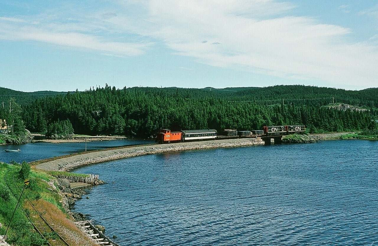 A special place – The Rock.
August 2, 1982.
Wonder Train. GMD built G-8's  #801-802 (with Caboose #6061) are in charge of the Weekly Wednesday only Clarenville – Bonavista Terra Transport train #206 at the causeway near Lockston on the approach to the Trinity Loop. (What's interesting: Yes, CN inherited a loop, constructed 1910 by the Reid Newfoundland Company, the loop is open unlike the covered loop in the west. (The closest existing “ near “ loop in the east that I can think of is Jackfish Bay on the CPR where – for example - the The Canadian's power would be proceeding in the opposite direction of the Park car. And of course in Pennsylvannia  is the horseshoe curve). Other “loops” you are aware of? See the Trinity Train Loop    http://www.heritage.nf.ca/society/rhs/tz_listing/155.html  ). The summertime train patronage was  sufficiently heavy that the crew had to use a caboose. Note the condition of the roadbed in the foreground and to the right of the roadbed the 1910 cribbing at sea level.)   Wondered why – in 1982 - why this train existed –  and certainly happy to witness and share with you. Kodachrome by S. Danko.