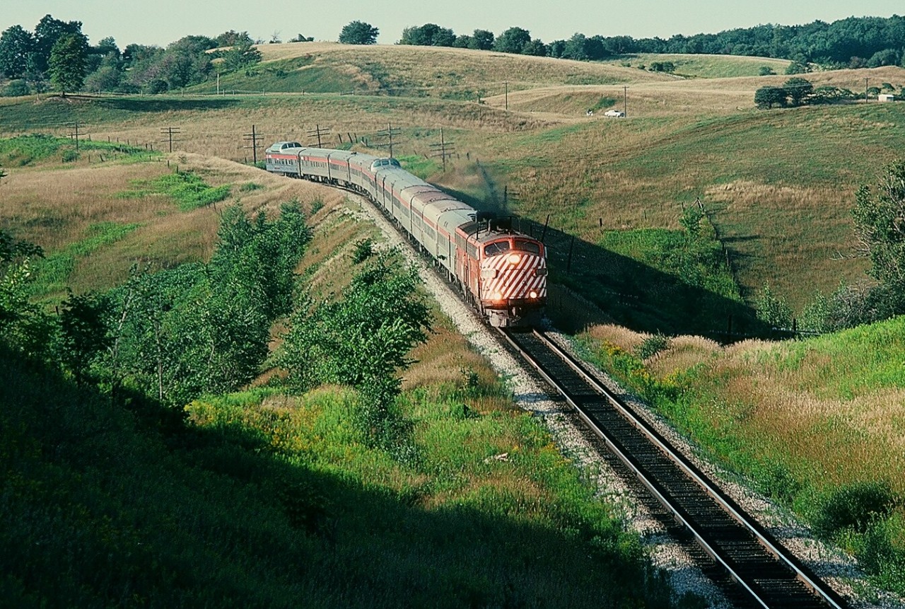 August 26, 1978 at the approach to Humber on the Mactier Subdivision in the Oak Ridges Moraine, an enormous CP Rail train #12, the Toronto section of The Canadian –  normally an eight car train – is a thirteen car train today! And only about one hour off the advertised. You are looking at the impact of an air traffic labour disruption (either a work to rule, lock out or strike – perhaps a viewer can clarify - for a week (or so) no regular passenger air travel). Both CP and CN had demand and ridership levels not experienced since the Centennial Year - 1967. What's interesting: It is rumoured that to re-position (ie send home) some CP Air crews the CP owned airline bought CP Rail tickets. CP Rail placed every available piece of passenger equipment, including the Angus Shop built 2200 series coaches, into service and on this train the Chateau sleeper in front of the Skyline Dome is in coach service. Look closely, the Vancouver originated equipment is coated in a fine layer of dust (see trailing image) while the Sudbury – Toronto only cars (the Skyline Dome, the Chateau sleeper in front of the Skyline and the Park car) are clean. It also appears that one of the 2200 series coach may have originated west of Sudbury. Certainly the FP7A #1432 (ex CP 4041) and the 1900 series F7B are getting a good workout. And at this location for the trailing image, an eight car train plus the power is easily in the whole frame, but today – surprise! And on the tail end the Park car is missing the drum head, likely sent to Montreal for sale by CP Archives - by October 1978 the train will be 'Via-ized'. Kodachrome by S.Danko.