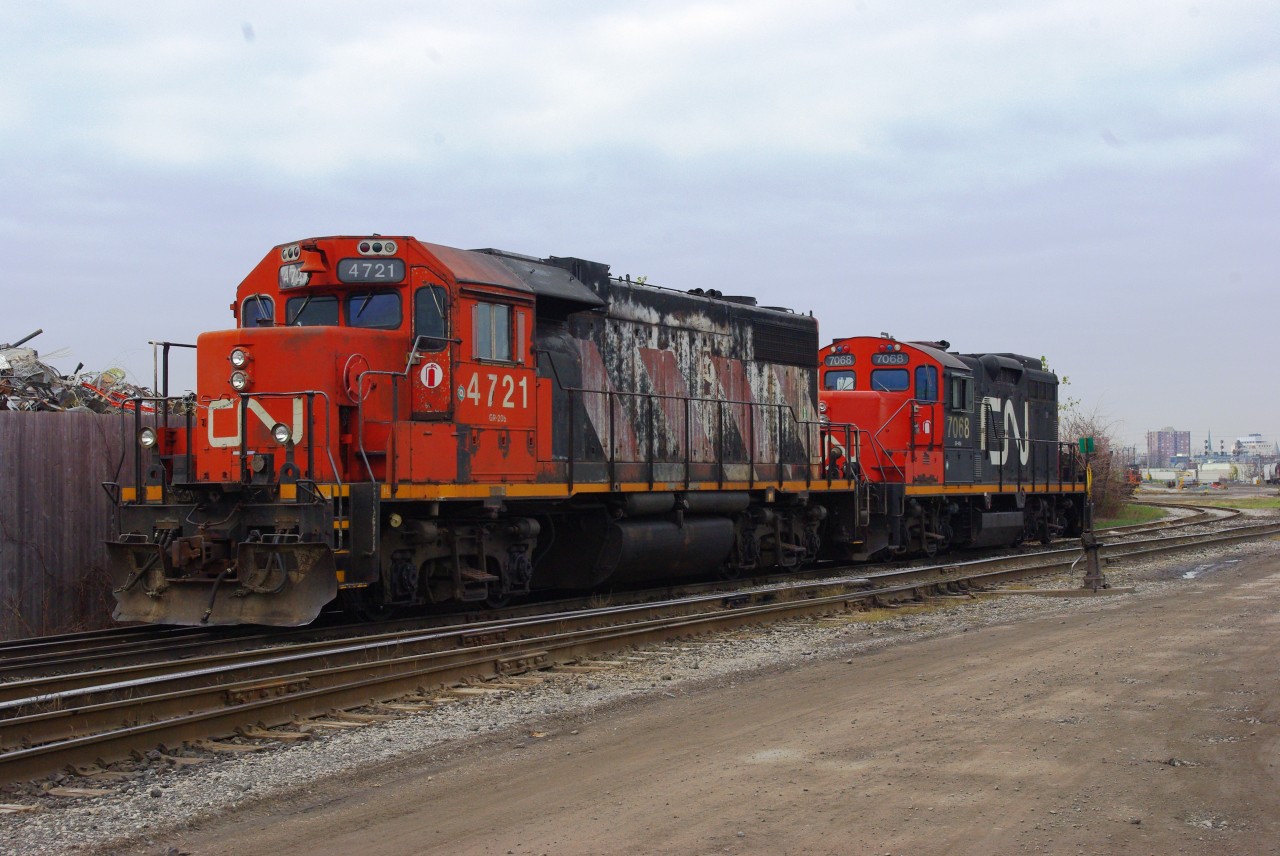 As she waits for a fresh crew to arrive, CN 4721 nervously eyes the scrap yard on the other side of the wooden fence.  Torches spark and grapples toss cut up iron right in front of this tired engines nose.