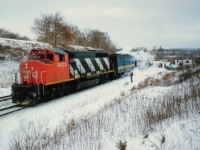 Well, here goes another puzzling situation. Rather than speculate, I will just note that this train westbound must be #75, with CN 9433 for power. However, it doesn't look like a #75. The next train west is #77 at 1755 which means it would have been in darkness. On the far right are Buddcars, the run to/from Niagara. However, the afternoon Budds are scheduled at 1423 at Burl. West, and #75 would be @1610, however it is not a scheduled stop.
So who and what is happening here at Bayview Jct.? The westbound is stopping and picking up passengers from the Budds. The autos in the photo are those of local railfans. Nobody got an explanation as to what transpired, as it was miserable and cold this last day of 1985. 
I believe the Budds were there when I arrived 5 minutes earlier, and if this is the Toronto bound train it would have been sitting there at least 1 1/2 hrs.