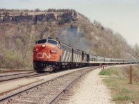   A glorious spring day at Dundas, a young mother and children have just climbed the hill by way of the Grindstone Creek viaduct and are waiting for this westbound CN passenger to pass. Power is 6534, 6623 and 4103.Despite it being only noonish, it is a very warm day. Direct center top is Dundas Peak where some great views of CN action can be noted.