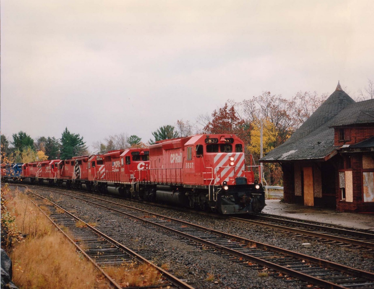 Northbound CP 5637,5587,3094,30xx,5680,5402,CRL(Conrail Leasing)600 and CP 5933 roar off the big Parry Sound trestle past the dilapidated old CP station, abandoned in early 1990; and was a potential firetrap until resurrected by an outfit that opened the Parry Sound Station Gallery in 2001. In this image the gloomy old station matched the weather of the late fall day,  cold and wet.
It was indeed a relief for the fans that the station survived all those years neglected without going up in flames as a result of vandals or vagrants. (Note wood pried off one lower bay window in photo)"The Sound" is one of the few communities in Ontario that can boast still having two railroad stations. The CN sta. is less than a mile away, serves as C of C and License Bureau.