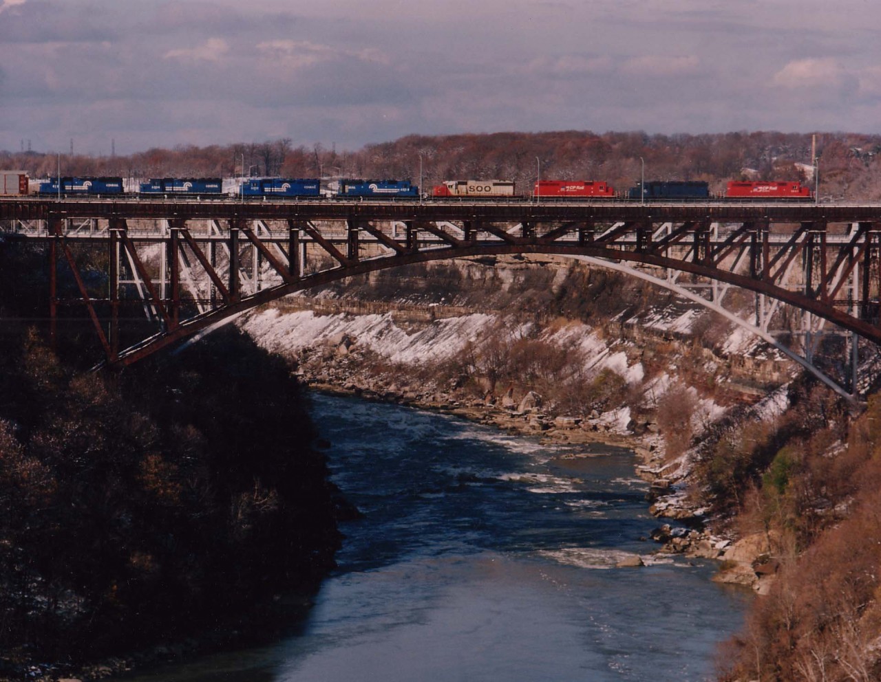 Shown here is the CP train #734 heading over the Niagara River via the old Suspension Bridge, now just a hulk too expensive to dismantle after the CP's line was pulled out of downtown Niagara Falls Ont in the late 1990s. Power this day is CP 5841, CRL 603, CP 751, SOO 6621 and CR 6308, 6322, 6304 and 812; these last four going off lease. CP had leased 24 SD40s back in the mid-90s from Conrail Leasing, and these were 4 of the first 12 to be returned by mid-November. Second unit in consist, CRL 603 (x-CR 6280)as well as another 11 Conrail Leasing units on the system remained until taken over by HELM (and renumbered)in the spring of 1996.
Photo taken at 1315 hrs on a windy but bright day.