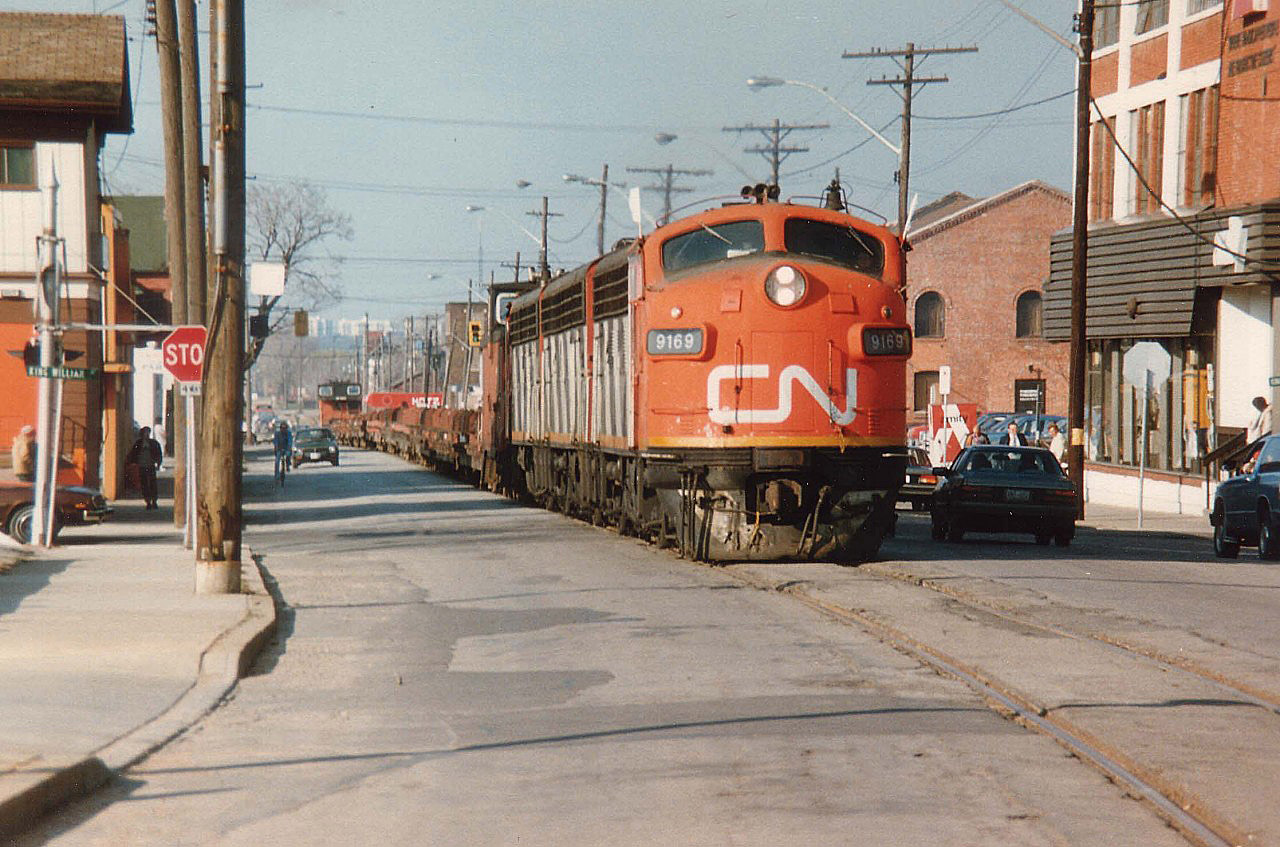 Even the locals are a bit awe-struck as CN's "Nanticoke" steel train rumbles up the middle of Ferguson Ave.N. in downtown Hamilton on its way up the hill thru Rymal, Caledonia, Hagersville and Garnet to the destination at the big steel facility on Lake Erie, about a 36 mile trip.
Power this day is CN 9169, 9196, 9172 with a rather short train. Caboose at each end so power can run around train upon return.