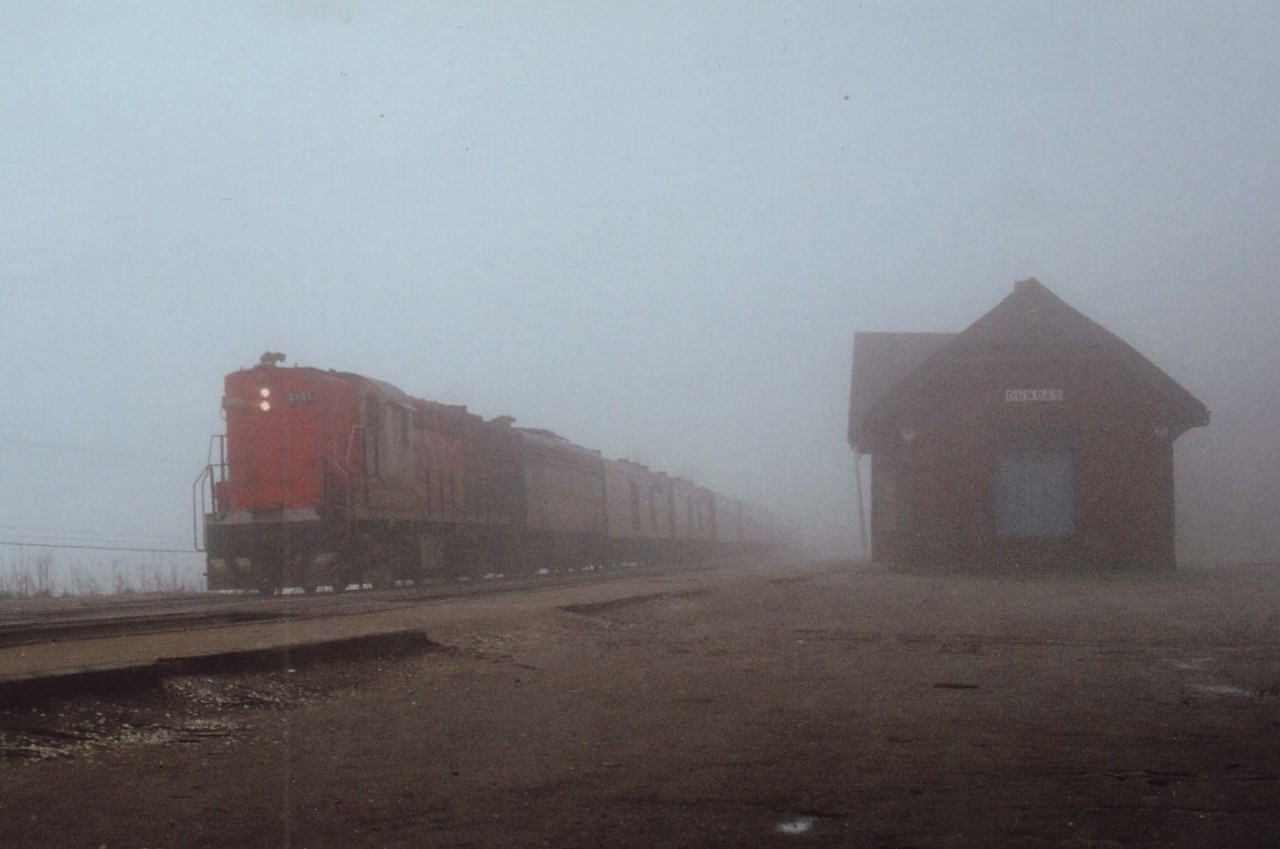 Fog-shrouded morning back on May 14, 1978 as CN's Tempo locomotive #3151 leads an eastbound #70 past the old station at Dundas. This station suffered a stove fire in 1986 which burned thru the roof and put the station permanently out of commission. The town could not come up with the moving/restoration expenses after CN offered them the building for the token $1 charge, and subsequently the building was razed.