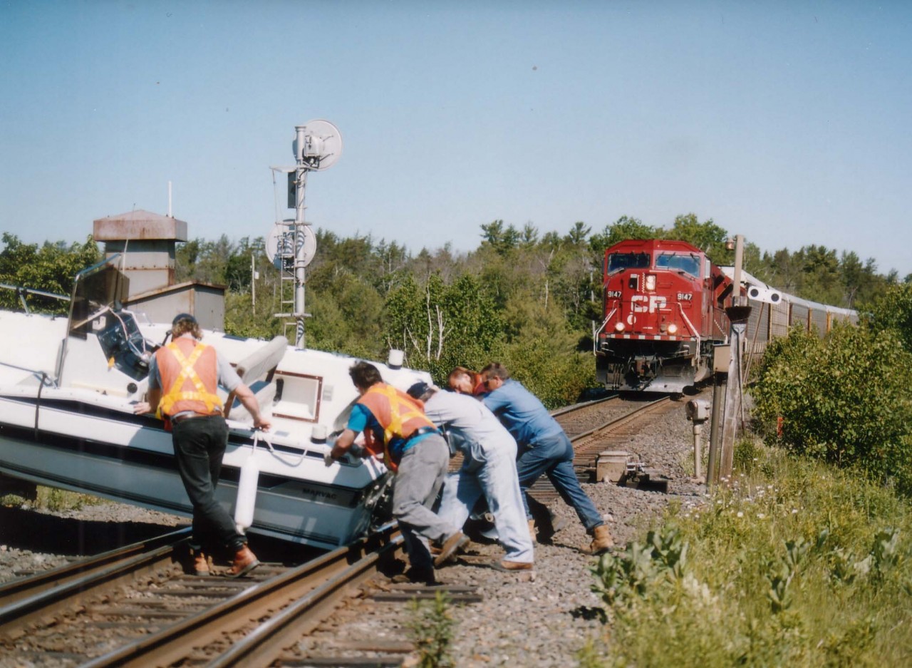 A close call for all concerned. Boat and trailer being towed up to the storage facility when the boat somehow broke loose, slid off the trailer, down the grade, and right onto the CP mainline. It was lucky a freight meet was coming up, the southbound CP 9147, 9156 was slowing up as the northbound was just taking to the siding. Crews from both trains, along with others locally tried to no avail to move the boat. In the end a fork lift from the marina had to come to the rescue.
