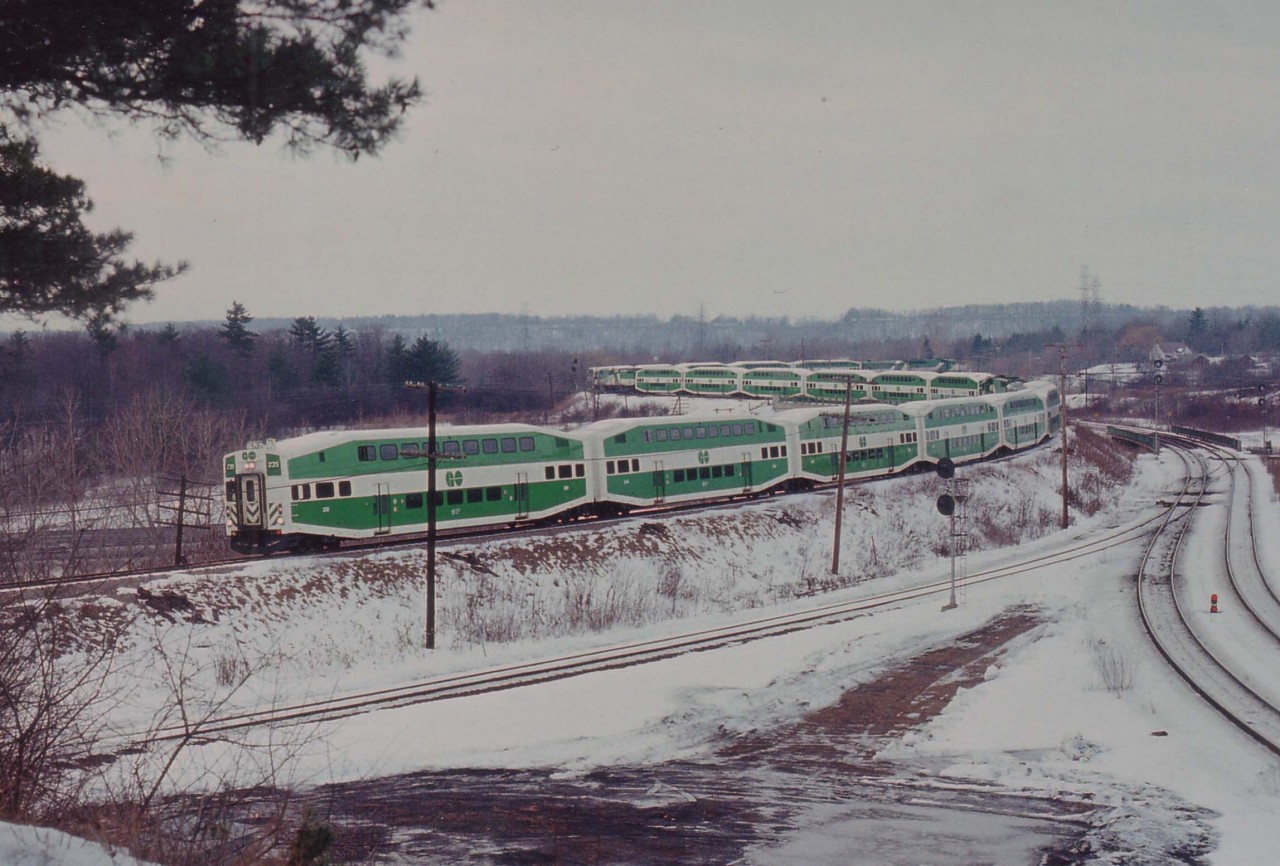 It appears to most of us the most interesting things happen on the crummiest days weatherwise. This is a classic example of a dull, grey day when an incident at Streetsville closed down the CP mainline and the GO sets, kept at the time by Guelph Junction, had no way to Toronto but to travel down the Hamilton Sub and head to Toronto in time for the afternoon rush by way of CN Oakville. (It was expected the line would reopen for the afternoon return) So here they all are: GO 239,904,721,510,907,906,and 705. (Should be 8?? I must have missed another cab in there somewhere)
The view is from the point overlooking CN Hamilton West and the train is crossing over Hwy 403.