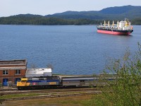 VIA's Skeena on its long layover at Prince Rupert sits by the derelict CN Station at Prince Rupert. A Chinese Grain freighter sits at anchor waiting a berth at Ridley Island Grain Terminal.  Via now uses the ferry terminal half mile south as its station and passenger loading area.,