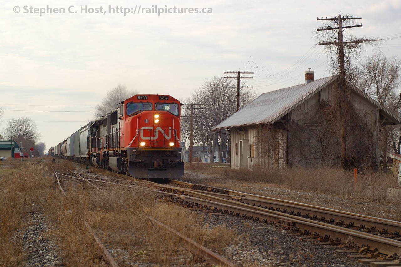 CN 434 (Windsor to Toronto manifest) is passing Comber Station with about 50 cars in tow. Comber Station is arguably one of, if not the oldest Wooden Railway stations in Canada still in railway service built in 1871. At the time this caption was written, the last train on the CASO is on the line and this section of track will shortly be a part of history.