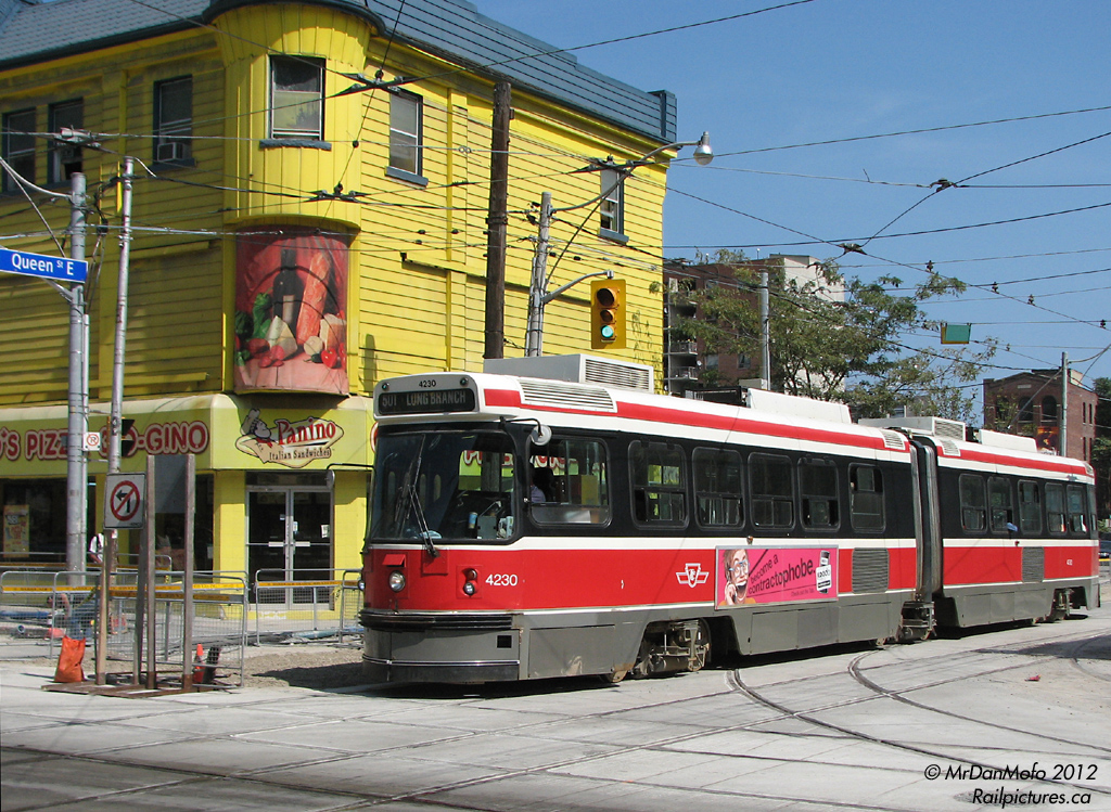 TTC Articulated Light Rail Vehicle (ALRV) 4230 rumbles westward across Church St. on a 501 Queen run, which had just resumed regular routing the day before. Note the relatively fresh in-pavement diamond(s) and the construction blockades: from July to early September 2009, the TTC rebuild its streetcar trackage along Church St. south of Carleton, beginning with rebuilding the intersection of Queen & Church. This necessitated detours of regular 501 and 502 cars (outlined here). While at this point most of the work is completed and regular Queen St. routing has resumed, there are still exposed switches to the north of the intersection that await paving over.