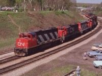 Eight units up front and 4 cabeese and (gasp) one load!  No doubt an equipment move westbound and one what looks to be a transformer along for the ride. A beautiful late May weekend has a few of the fans out at the Jct., a most popular location for trainwatching many years back.
Only locos noted are the first 4, CN 5570, 5506, 9574 and 9521............