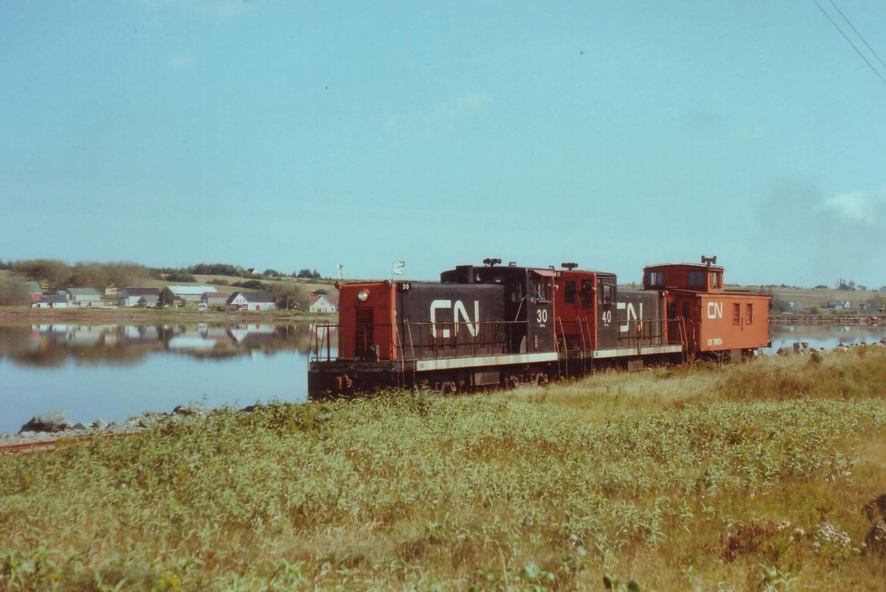 A couple of CN's vintage 70 tonners are seen here drifting westbound past St. Peter's Bay thru the idyllic countryside. CN #30 and #40 both retired after CN abandoned the Isle in the early '80s; the #30 is on isplay at Delson, QC. This train is returning to Charlottetown after taking a few cars out to Souris for the potato harvest.