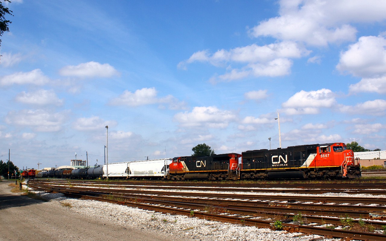 On a warm sunny day, CN 509 starts into Racecourse yard after their trip from Sarnia. In the distance at left, the Racecourse yard job crew is tied down as the crew is on lunch, and a second set of geeps sits on the back lead; being a Sunday, there is no 584 so they have the day off.