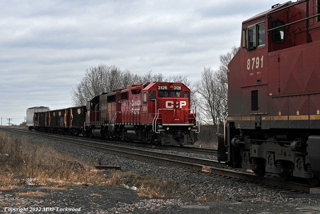 Performing a rolling meet, CP trains T25 and 112 pass at Lovekin. T25 behind CP 3126 and 4657 will stop to work the backtrack, picking up two rail flats which will join the already awelled consist of five ballast hoppers from the Newtonville pocket track and what looks to be a revenue car out of Cobourg.CP 8791 and 8567 power 112. 1453hrs.