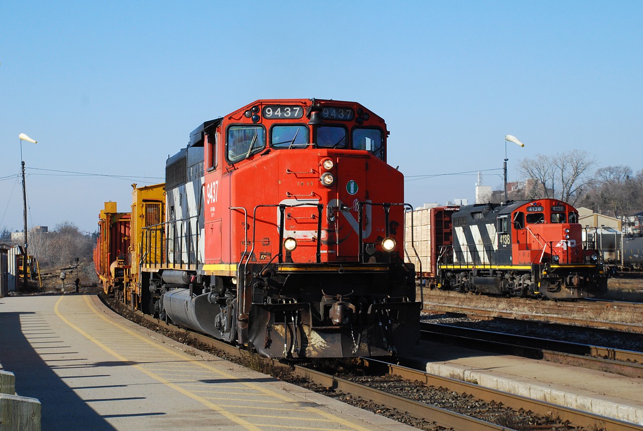 CN 9437 leads a loaded rail train past "AR Illinois" 4138 parked in the yard.