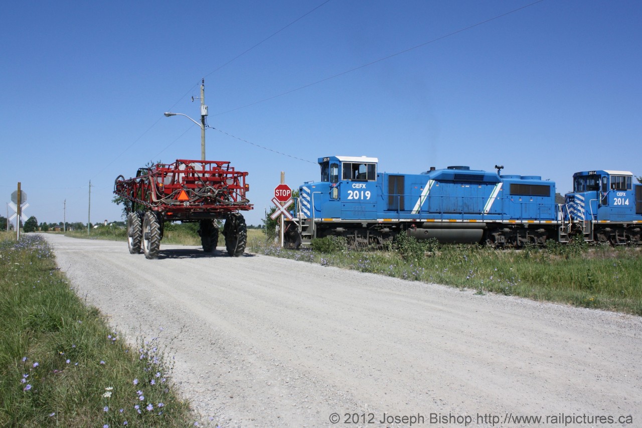 A farmer makes what would appear to be a very dangerous move at a crossing in Garnet Ontario.  In reality the train is backing away from the crossing and the farmer is not putting himself at risk at all.  This photo was taken at the SOR yard at Garnet Ontario