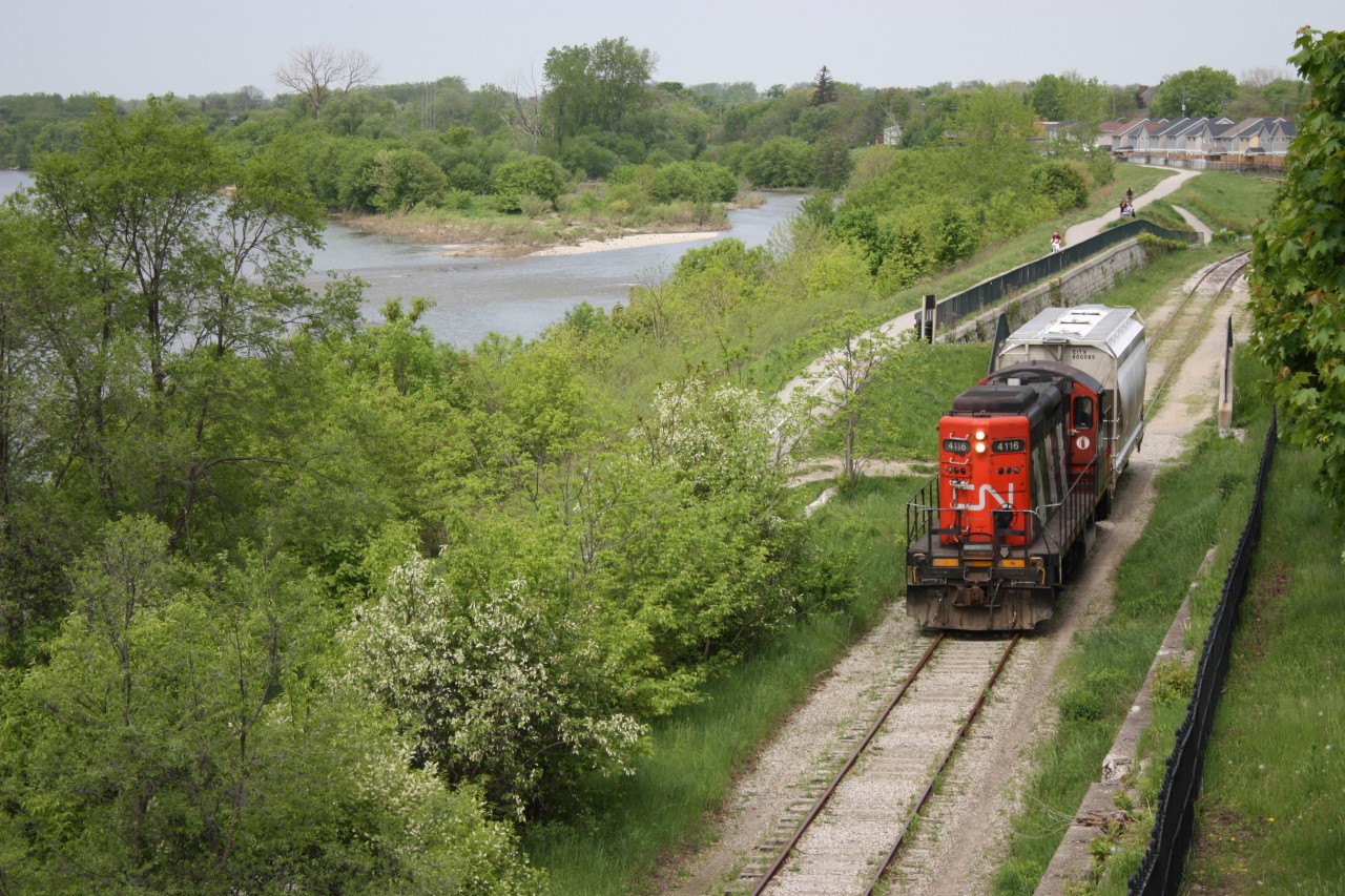 CN #580 with a lone covered hopper in tow passes the flood wall along the Grand River at Brantford on the Burford spur (ex LE&N portion). The train is returning after working SC Johnson & Son at the end of the line. The LE&N car shops at one time occupied the land near the new housing development in the background.