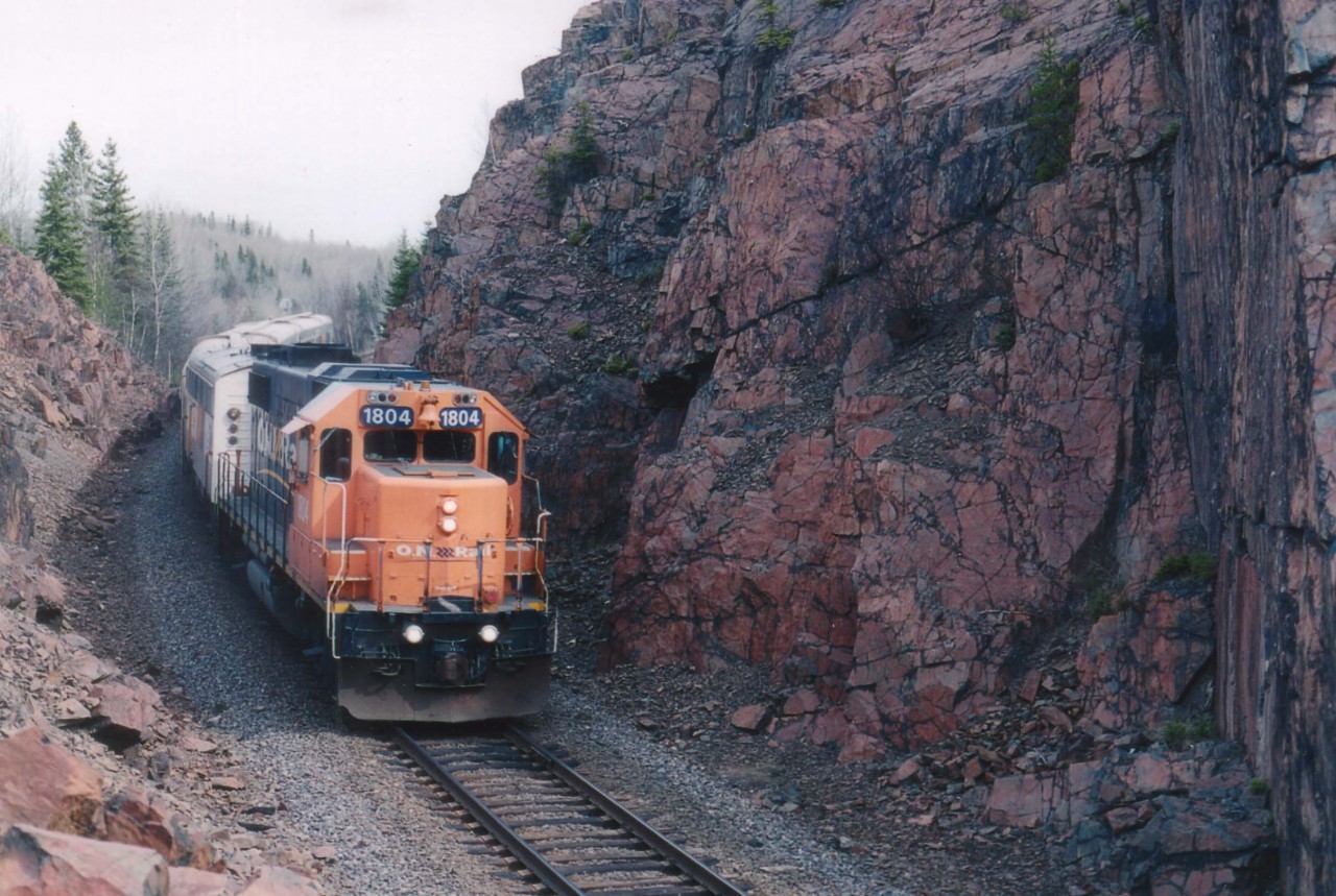 Much has been written over the years about the mining in the ast central part of Northern Ontario, but little known to railfans is Boston Creek, amongst the most storied areas of them all.  The location is now just an unincorporated hamelet of a handful of ramshackle houses at the end of a dead end gravel road.  The ONR skirts thru the west side of it, and a drive in produced this shot of ONR 1804 about to enter thru the cut just north of the roadway. This is a territory in which to make sure you have your 'bug netting', every flying object around here seems to be overly hungry. ONR 1804 and 204 are on the head end today, a warm spring May 13, 2005; which accounts for all the bugs. After this train passed, it was a race for the car. How the moose can stand it, I don't know.
The famed Adams Mine is located not far north of here.