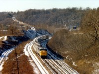 This is my favourite image taken at Dundas. A very unusual angle; looking west toward the old Dundas Station (demo'd in 1986)and the MoW shanty, as well as a few automobiles to prove the location was not yet totally devoid of customers.
Track on left siding for stone cars from CCSL (now shut down) and possibly Steetly, which operated at this time a small crushed stone and gravel business. Off to the far left is the Steetly connection, lifted in the mid 1980s.
Lead unit on #72 is VIA 6786. Location from where this image was taken, the CCSL conveyer overhang, was dismantled in 1989, according to my notes.