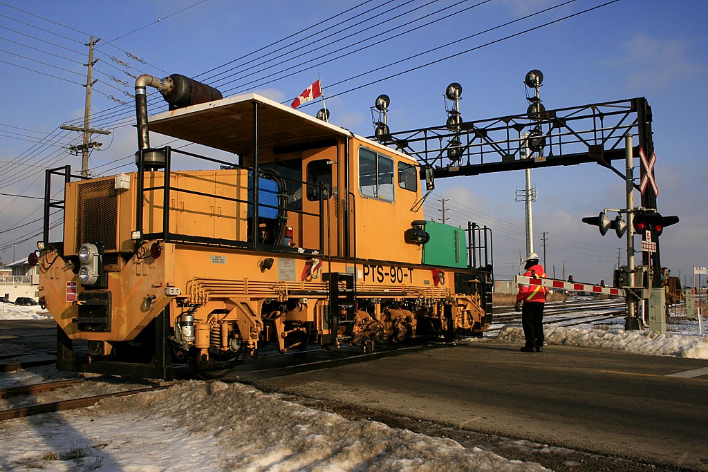 A Plasser Dynamic Track Stabilizer, part of a long parade of maintenance equipment departing Oakville Yard this day, crosses over Chartwell Road heading west.
