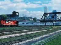 Tempo Train. CN's 1968 effort to modernize the south west Ontario passenger service. Built by Hawker Siddeley in Thunder Bay (at the former Canadian Car & Foundry (Can Car)) plant (at one time part of the A.V.Roe manufacturing group (and that is a story unto itself!)) the original all aluminum construction five Club cars, five Cafe coaches and fifteen coaches (three hundred series) were essentially modified H series TTC subway cars (as were the original low level GO Transit coaches). The Tempo equipment was as modern as the Turbo, however Via could not seem to find a way to continue to include this modern electric heated (and air conditioned) aluminum fleet - by 1982 the Tempo's were replaced (in the timetable) by Rapidos' and (date?) the Tempo fleet was eventually sold to the D&RGW (for Ski Train operation). (Perhaps Via was optimistic that the LRC would be an adequate replacement ? ! ). Recently (2009 ? ) the Tempo fleet - now at 45 years - is back on CN for the Agawa Canyon service! For power, in 1968 CN modified six RS-18's (3150 to 3155) with electric generators plus modified three baggage cars (15300-153020) with generators - all retired by 1983. Given this June 1977 date the Tempo Train here is likely the equipment for Club Car equipped Via CN train #73 or #75. Kodachrome by S. Danko.

