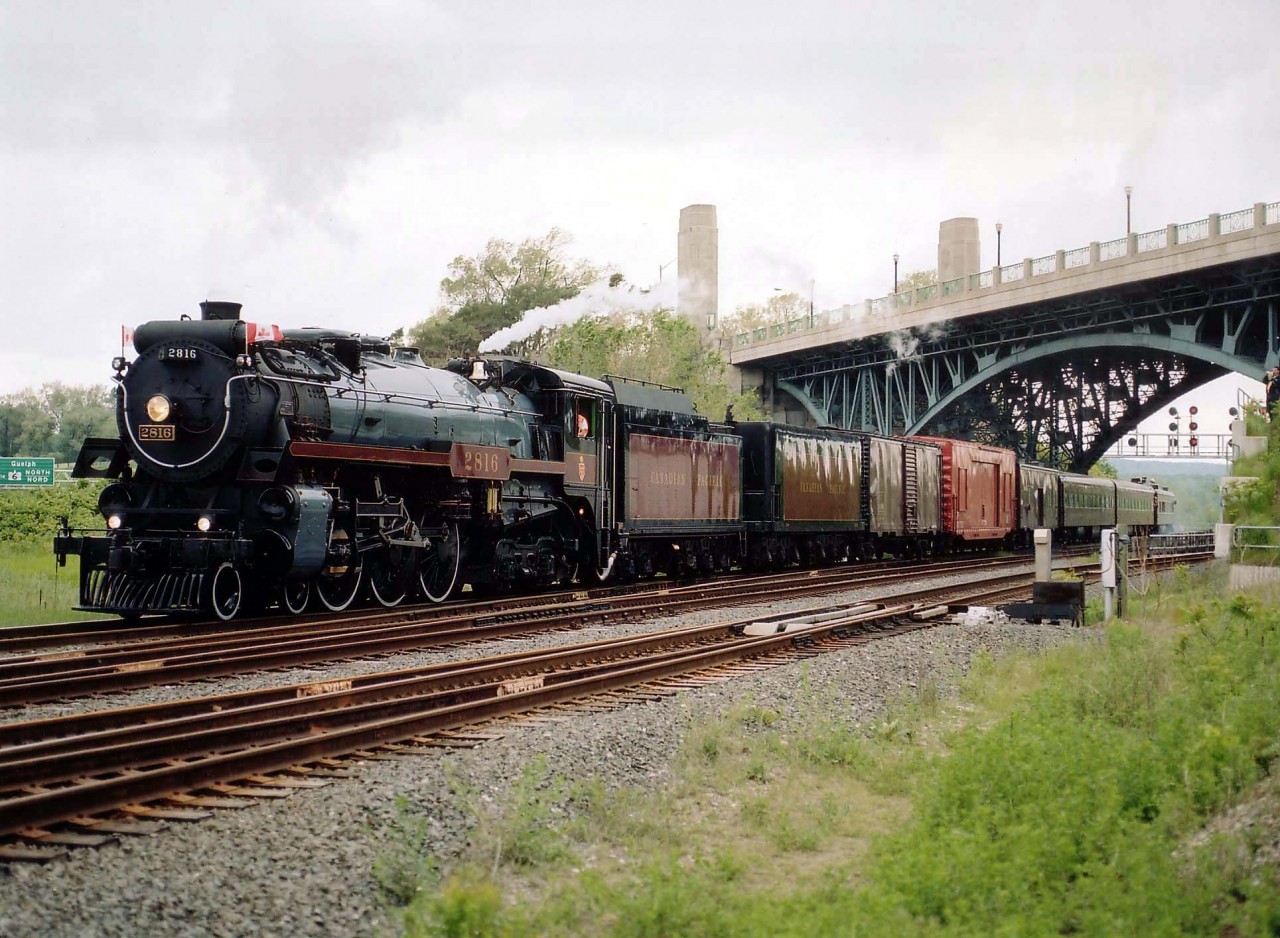 It was June 2003 when CP's grand old steam engine 2816, touring Canada, made the rounds in Ontario, having run southbound over the big Parry Sound bridge on June 5th and returning north over same on June 22nd. It was a month when all the train nuts were foaming in overdrive. This one was rather bad as well. :o)  The handful of fans who ventured out around the High Level Bridge at the west end of Hamilton became increasingly disappointed as the prevailent sunshine disappeared and a cloud provoked drizzle took over while the train was delayed somewhere up the line around Waterdown due to fallen trees, of all things. Speculation of vandals in action was the general feeling, but I never did find out what happened. Anyway, it all worked out in the end and the train put on a grand show as it rolled by; this photo now a treasure in the sense that latest rumour has it CP has the old 2816 up for sale. We may never see it run in Canada again.  A huge loss.