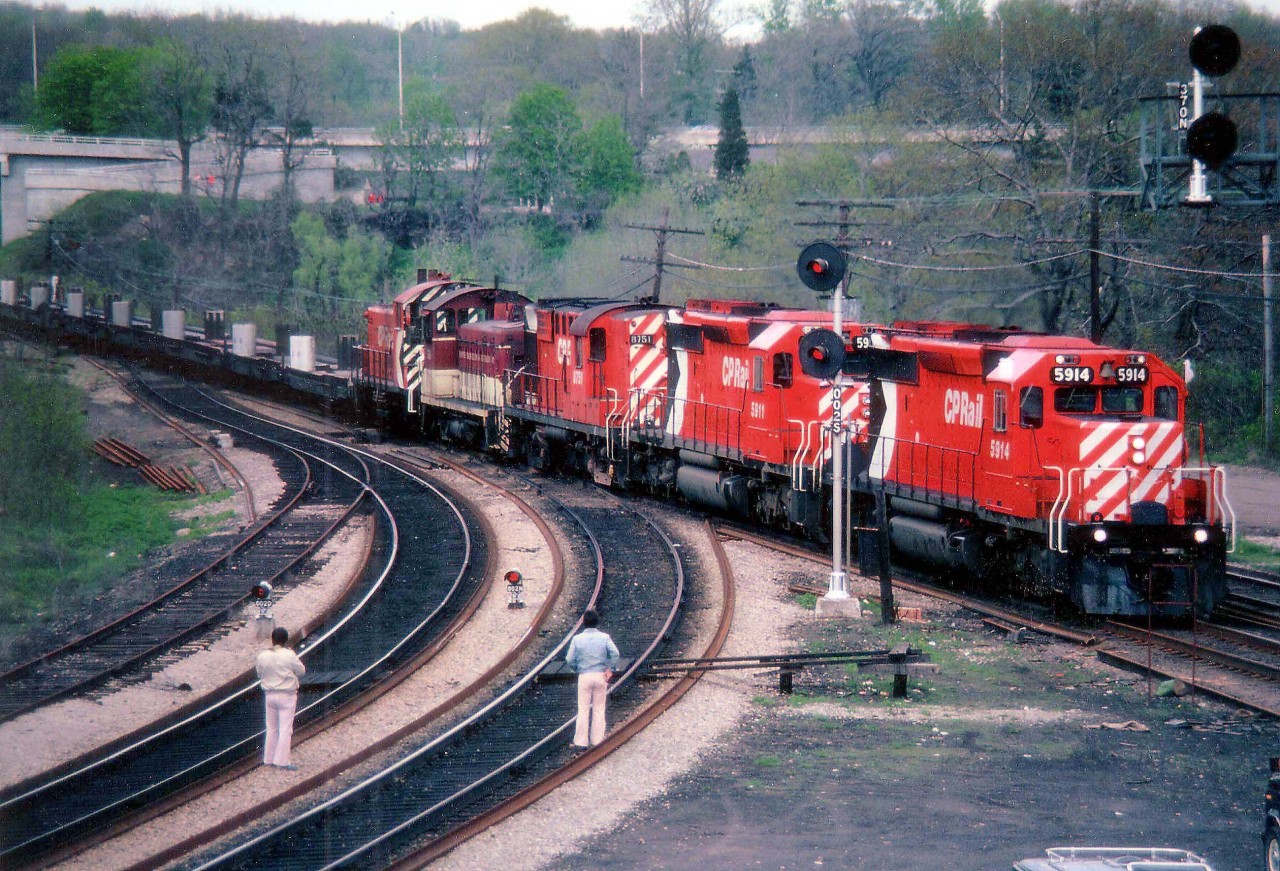 CP 5914 and 5911 are but 5 months old as witnessed in this May 13, 1979 view of the TH&B "Starlite" rolling Hamilton-bound thru the junction at Bayview. Other locomotives are CP 8751, TH&B 56 and a CP 81xx trailing. One has to express curiosity as to why railfans would wear almost white !!! clothes when out amongst the grease and the grime of the railway landscapes........and indeed why they are chancing the location that they are. Times and styles have changed. Railfans used to have the run of many locations without interference from authority. All this has a thing of the past, but many fans have not changed along with it. (How many have ever been hurt or killed while railfanning, would be an interesting statistic)
Incidentally, the rusted track on the left is from the days when steam engines waited to assist westbound trains up the Dundas grade, a hold-over only because in the 1970s MoW equipment used this stub. The track has long since been removed.