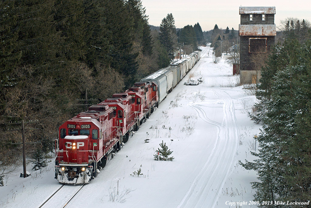 I'm posting this shot to show a more contemporary view from the Hwy 35 bridge at Pontypool. Almost 27 years after S Danko's view of VIA 189 flying through town, CP 3105, 3045, 8200, and 3042 plod through at 10mph with T07's train. The siding, obscured by snow, remains, though it is now stub ended with the wheelstops located at the bush below the crossbuck. The elevator still stands, and indeed is seeing a slow restoration by locals, though the office section seen in the earlier shot is now but a crumbling foundation. The trees have grown much in the intervening years. And the railroad runs a few round trips to Toronto per week, under the guise of the Kawartha Lakes Railway internal shortline, at a relaxed pace, down from six per week in the eighties. 0910hrs.