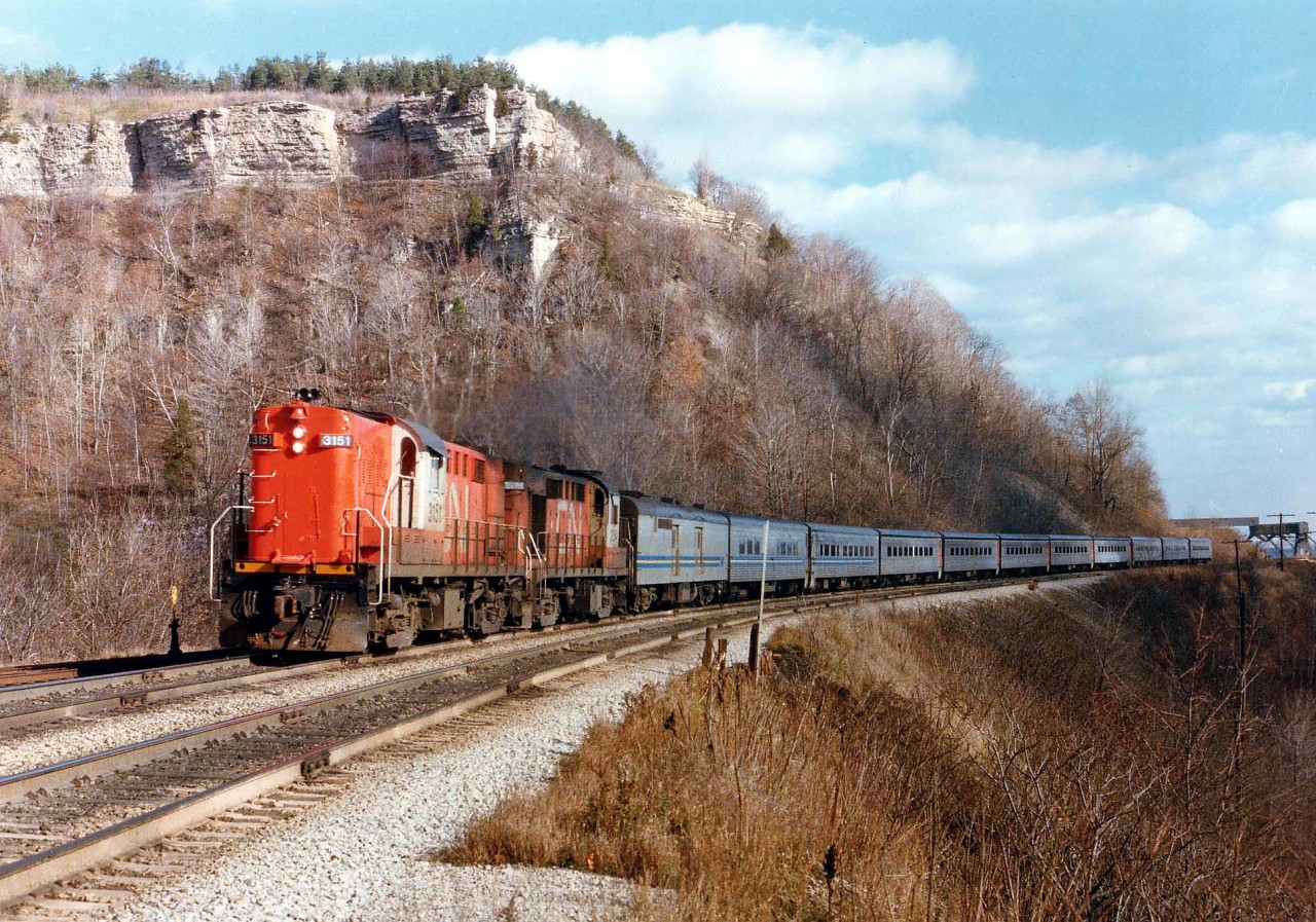 VIA Rail is still in its infancy and it is rather obvious as CN Tempo units 3151 and 3154 are powering an eleven car westbound approaching Dundas Station. For those familiar with this area, note the "guardrail" up at the Peak Lookout. And note the CCSL conveyer is still intact, seen at the extreme right of the photo.