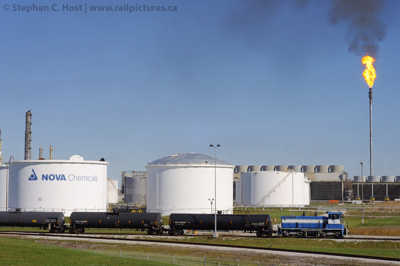 Flare up:  Nova Chemicals SW1200, probably #902 is switching the large facility near Mooretown, Ontario. A large flare is burning in the background - these large flares are rather rare especially during the daytime hours. You could see this burning for over 30 KM. Consider the size of the flare, distance away from the locomotive and photographer - it is easily over 50 feet tall. Photo taken from public property (Nearby road)