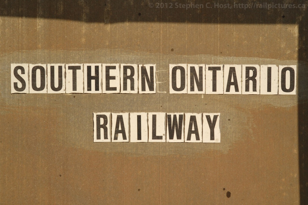 Lunch Room  - this is not the official logo for the Southern Ontario Railway - for North Hamilton it certainly looks the part. These words demarc the Lunch Room for the Southern Ontario Railway - or at least, you think it was used as a Lunch room. A small green Steel structure (fitting for Steeltown) with heavy wire protecting the windows, and a steel roof - akin to a bomb shelter. Perhaps the description fits the surroundings - the dimunitive structure dwarfed by towering Dofasco facilities: 10+ story Dofasco head office, Dofasco manufacturing, coil storage, and water treatmaent facilities which arch over Ottawa St in a menacing "Abandon hope all ye who enter here" way. Heavy rubber tired vehicles passing on the minute filled with 200+ tons of red hot steel coils from the rolling mills, and of course, plenty of dust.
Next photo will depict train traffic...