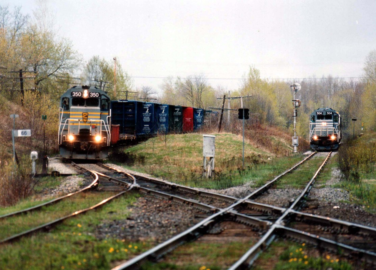 Two trains meet at the Lennoxville diamond. Quebec Southern Rwy 504 and 500,at Sherbrooke Sub., wait for thru freight BAR 350, AMTK 387 and HATX 176, a Canadian-American Rwy (CDAC) train on QSR trackage, mile 66. It will cross the diamond eastward and will then be travelling on CDAC rails. The QSR local is on CN Sherbrooke Sub. trackage. The in and out sun, a fixed lens and the general lay of the land made this a difficult place to shoot.
At this time CDAC was part of the Bangor & Aroostook system (BAR).