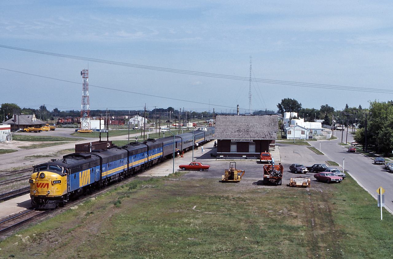 VIA #1 preforms their station stop at Portage La Prairie with an A-B-B-B providing the horsepower, in the background a CP westbound rolls through town towards the diamond.