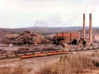 From high on the rocks, here is an overview of the great Sinter Plant that used to provide so much employment to the town of Wawa, Ontario as well as the former Algoma Central Railroad. The purpose of the plant was to supply blast furnaces with sinter, a combination of blended ores, fluxes and coke which is partially "cooked" or sintered. In this form the materials combine efficiently in the blast furnace and allow for more consistent and controllable iron manufacture. From here, material was transported out to Michipicoten Harbour, about 12 miles west, for GreatLakes shipping. Awaiting next assignment are WC 6604, 6655, 3012 and 6506. The F45, 6655, was retired in 2002. Later on this year 1998 the plant was closed, buildings removed, track removed, and nothing is left but a blight on the landscape.  The plant had been in continuous operation since 1939, and is now but a memory.