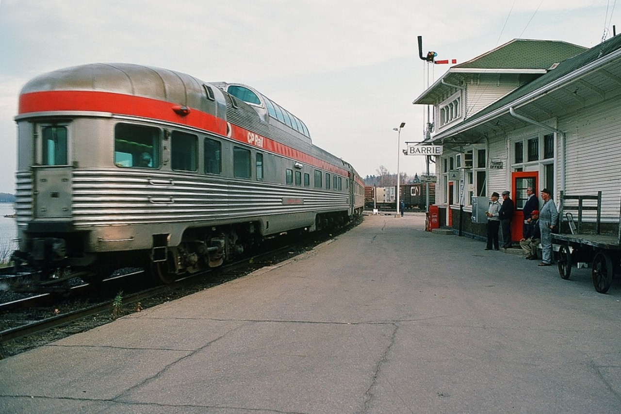 The local observers are bemused by the appearance of a CP train at the CN Barrie station: After the station stop, one two hundred fiftieths of a second is insufficient to freeze frame the acceleration provided by the aging ex CP Rail F units ( 1432 – 4477 – 14xx ) pulling the newly re-routed VIA Rail train #2. 

Effective October 29, 1978  Via Rail ceased service on the CP Rail Mactier Subdivision and re-routed the transcon service onto the CN ( at CN Boyne – from CP Reynolds ) Bala Subdivision (north of Washago) and onto the CN Newmarket Subdivision south of Washago.

(What's interesting: note the station signal board controlled by the station operator)

November 1978. Kodachrome by S. Danko.

more at Barrie:  ex CP Rail Brook Manor at the ex GTR station 

sdfourty.